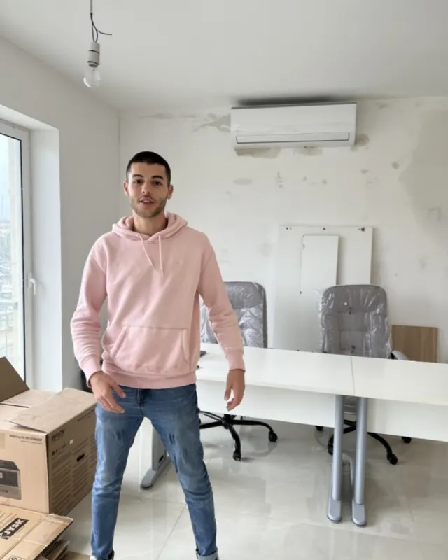 Stephen in a pink hoodie standing in an empty new office, November 2021