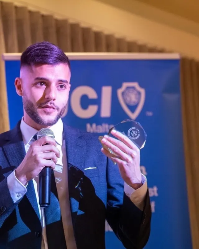 Stephen holding a microphone and a glass award at JCI Malta, November 2023